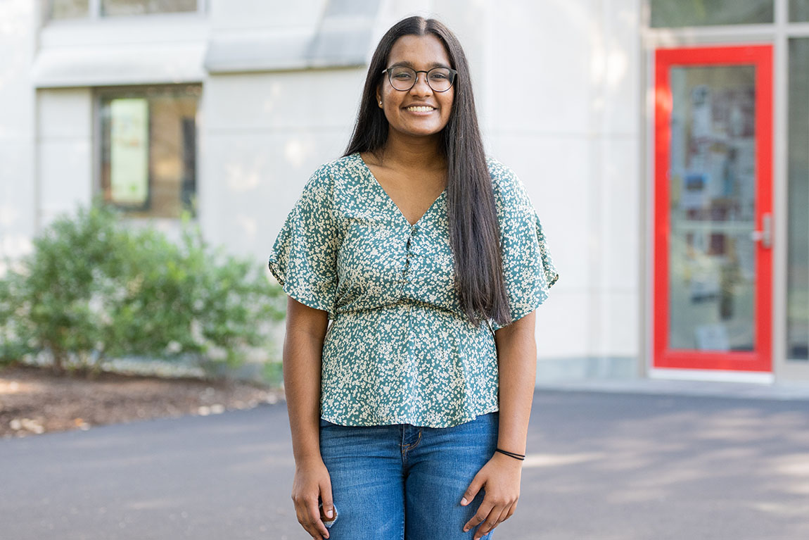 A smiling student wearing glasses outside an academic building